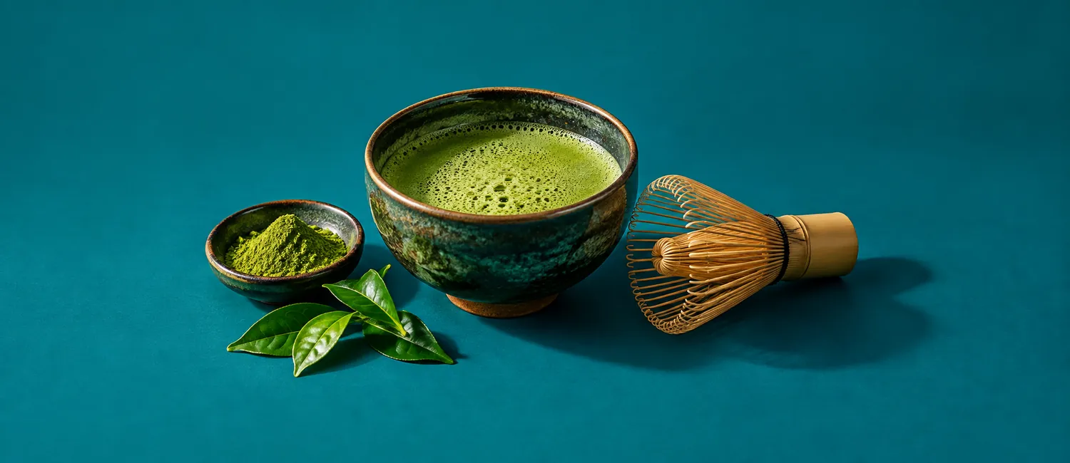 Skål med grön matcha och bambuvisp mot tealfärgad bakgrund