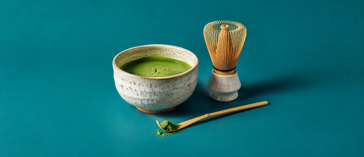 Skål med nyvispat matcha te och en bambuvisp mot blågrön bakgrund