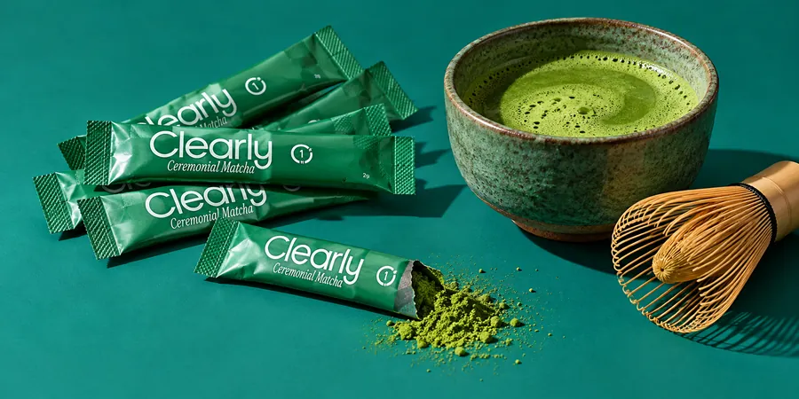 Clearly Matcha i förseglade stickor bredvid en skål med matcha mot blågrön bakgrund